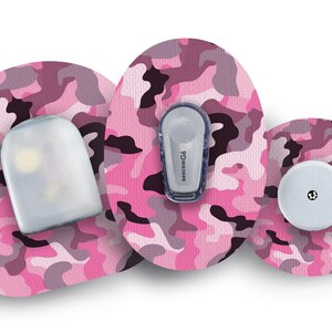 May include: Three pink and black camouflage patterned adhesive patches for a medical device. The patches feature a round shape, an oval shape, and a rectangular shape. The oval patch has the text "dexcom G6" printed on it.