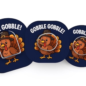 Peut inclure: Trois autocollants circulaires bleu foncé représentant une dinde de dessin animé portant un chapeau de pèlerin marron. Chaque autocollant affiche le texte GOBBLE GOBBLE! en lettres capitales blanches. Les dindes ont des plumes marron.