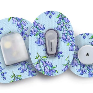 May include: Medical devices with floral patterned adhesive patches. The patches are light blue with purple and green floral designs. The devices include a sensor, transmitter, and a white round component.