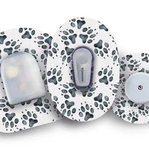 Puede incluir: Tres parches médicos redondos con un patrón de huellas de patas. Los parches son blancos con huellas de patas negras. El parche central tiene un pequeño botón redondo blanco con un punto negro en el centro. El parche de la izquierda tiene un dispositivo rectangular transparente con una etiqueta blanca que dice "dexcom G6". El parche de la derecha tiene un dispositivo rectangular transparente con una etiqueta blanca que dice "dexcom G6".