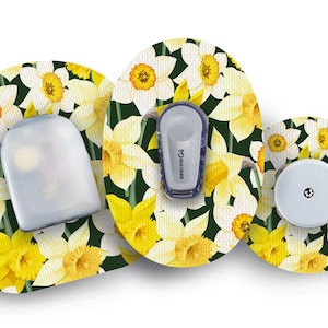 May include: Three medical devices with a floral design. The background features a pattern of white and yellow daffodils on a dark green background. The devices include a sensor, transmitter, and receiver.