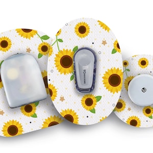 Könnte beinhalten: Drei runde Klebepflaster mit einem Sonnenblumenmuster. Die Pflaster sind weiß mit gelben Sonnenblumen und grünen Blättern. Ein Pflaster hat eine transparente Plastikabdeckung, eines hat einen kleinen weißen runden Sensor und eines hat ein kleines blaues und weißes Gerät mit dem Text "dexcom G6".