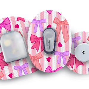 May include: Three medical devices with a pink bow and heart pattern on a white and pink striped background. The devices include a sensor, a transmitter with the text "dexcom G6", and a white receiver.