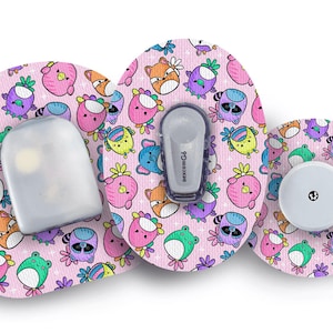 Puede incluir: Parches adhesivos rosas con un patrón repetido de animales de dibujos animados, incluyendo zorros, mapaches y pájaros. Los parches están diseñados para sujetar dispositivos médicos, con un sensor y un transmisor visibles. El diseño es colorido y juguetón.