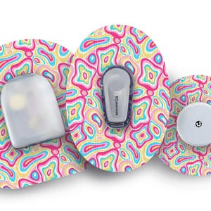 Op de afbeelding: Drie kleurrijke ronde medische apparaatpleisters met een wervelend abstract patroon in roze, geel, blauw en wit. Eén pleister heeft een doorzichtige plastic afdekking, één heeft een kleine ronde witte sensor en één heeft een grijze sensor met het woord "Dexcom" erop gedrukt.