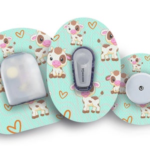 Puede incluir: Tres parches redondos adhesivos con un fondo azul claro y un patrón repetitivo de vacas de dibujos animados marrones y blancas con narices rosas y ojos marrones. Los parches tienen un borde blanco y un patrón de corazones marrones. Un parche tiene un depósito de plástico transparente, otro tiene un sensor redondo blanco y el último tiene un dispositivo rectangular gris con el texto "dexcom G6" impreso en él.