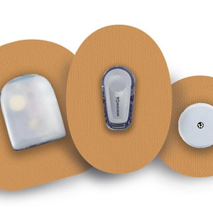 Op de afbeelding: Drie ronde pleisters met een witte, grijze en transparante sensor op elk. De pleisters bevinden zich op een bruine achtergrond.