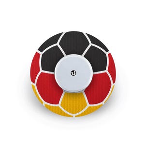 Könnte beinhalten: Ein kreisförmiges Klebepflaster mit einem Fußballmuster aus schwarzen, roten und gelben Segmenten, die durch weiße Linien getrennt sind. Ein kleiner, weißer, runder Sensor mit einem winzigen schwarzen Symbol in der Mitte ist mittig angebracht.