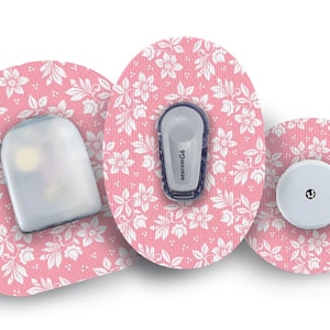 Könnte beinhalten: Drei runde medizinische Pflaster mit einem rosafarbenen Blumenmuster. Die Pflaster sind für ein kontinuierliches Glukose-Monitoring. Das mittlere Pflaster hat einen kleinen, runden, weißen Sensor mit einem schwarzen Punkt in der Mitte. Das linke Pflaster hat einen durchsichtigen, rechteckigen Sensor mit einem kleinen, weißen Licht. Das rechte Pflaster hat einen kleinen, rechteckigen, grauen Sensor mit dem aufgedruckten Text "FreeStyle Libre".