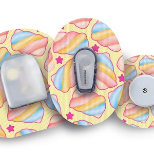 Può includere: Tre cerotti rotondi e colorati per dispositivi medici con un design fantasioso che presenta vortici rosa, blu e gialli su uno sfondo giallo con stelle rosa. I cerotti sono progettati per coprire un dispositivo medico.