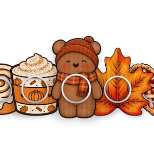 May include: A set of five circular white plastic buttons featuring autumn-themed illustrations: a cinnamon roll, a pumpkin spice latte, a brown teddy bear wearing an orange beanie and scarf, a large orange maple leaf, and a heart-shaped cherry pie.