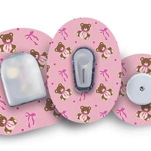 Peut inclure: Trois patchs adhésifs roses et blancs avec un motif répété d'ours en peluche bruns portant des nœuds roses. Les patchs sont conçus pour les dispositifs médicaux.