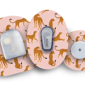 May include: Three round adhesive patches with a pink background and a repeating pattern of orange and brown cheetahs. The patches are designed to cover medical devices. One patch has a clear plastic cover, one has a white round sensor, and one has a small grey device with the text "dexcom G6".