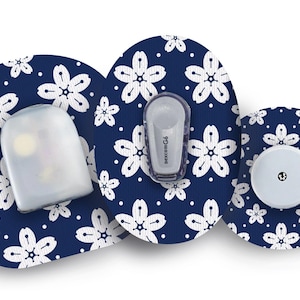 Op de afbeelding: Drie ronde medische pleisters met een blauwe achtergrond en een wit kersenbloesemmotief. De pleisters hebben verschillende formaten doorzichtige plastic afdekkingen met een klein wit stipje in het midden.