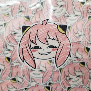 May include: Anya Forger sticker featuring a pink-haired character with a mischievous expression. The sticker has a black outline and yellow accents on the ears. The background is filled with similar stickers.