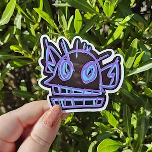 May include: A black and white sticker with a purple outline of a cartoon monster with large eyes. The monster has a toothy grin and a series of lines around its head.