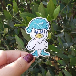 May include: A blue and white cartoon duck sticker with a blue hat and a yellow beak. The duck is wearing a blue hat with a white stripe and has a white body with blue feet.