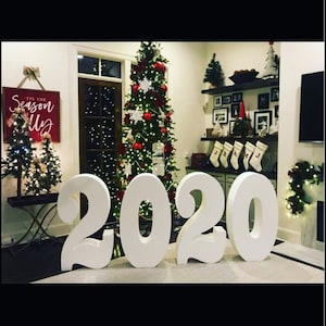 Puede incluir: Números de espuma blanca que deletrean "2020" en un ambiente festivo con un árbol de Navidad decorado con adornos rojos y copos de nieve blancos.