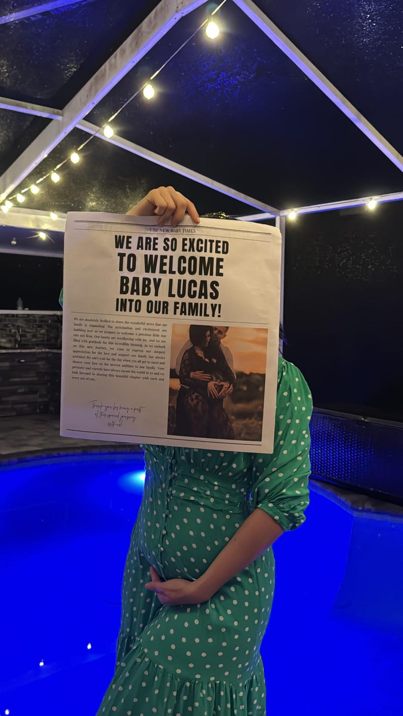 May include: A woman in a green polka dot dress holds a newspaper announcing the birth of "Baby Lucas" with the headline "We are so excited to welcome Baby Lucas into our family!" The newspaper features a photo of a couple holding hands with the woman's hand on her stomach.