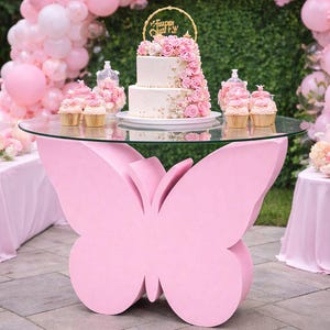 May include: A two-tiered cake with pink roses and a gold topper that reads "Happy Birthday" sits on a glass-topped table with a pink butterfly base. Cupcakes and pink balloons decorate the party setting.