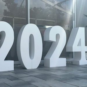 Puede incluir: Números de espuma blanca que deletrean el año 2024. Los números son grandes y se encuentran en un suelo de baldosas grises.