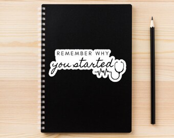 Könnte beinhalten: Schwarzes Notizbuch mit einem weißen Aufkleber, auf dem "Remember why you started" steht, mit einem Stethoskop und einer Herzfrequenzlinie.