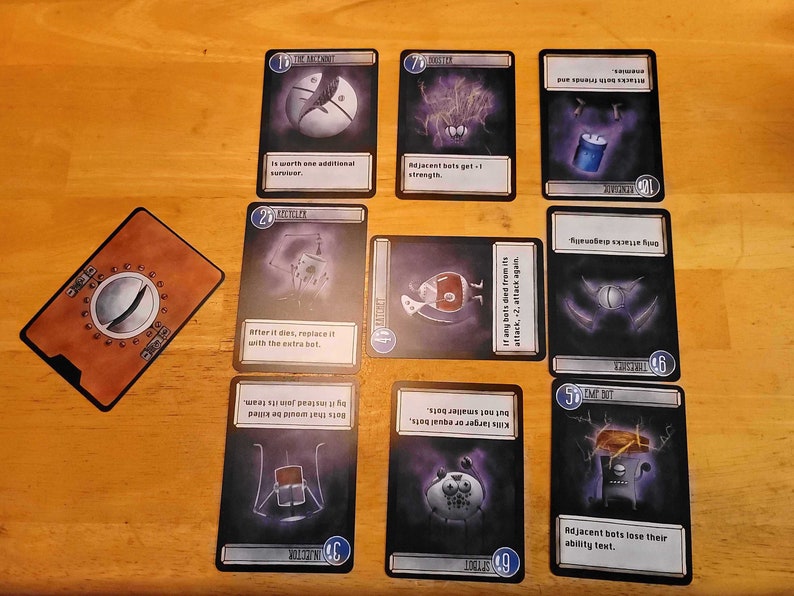 May include: A tabletop card game with illustrated cards featuring robots and abstract designs. The cards have text descriptions and numbers. A brown card with a metallic design is also present.