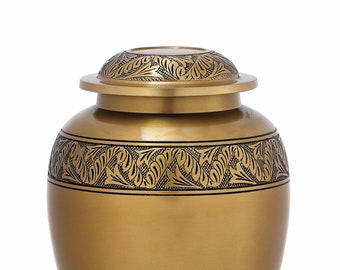 May include: A gold metal urn with a decorative floral pattern. The urn has a lid and a base.
