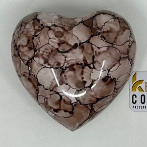 Puede incluir: Una urna de cremación de cerámica en forma de corazón con un diseño marmoleado en tonos marrones y blancos.