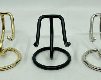 May include: Three metal display stands for small objects. The stands are made of gold, black, and silver metal. Each stand has a round base and three curved arms.