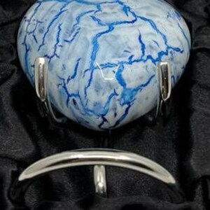 May include: A heart-shaped agate cremation urn with a blue and white marbled pattern. The urn is displayed on a silver stand.