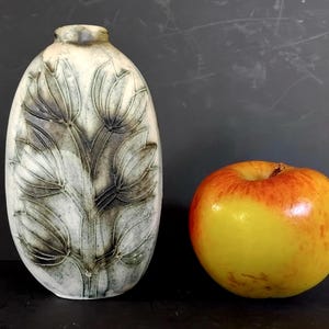 May include: An oval ceramic vase with a floral pattern and a yellow and red apple. The vase has a light base and a dark floral design. The apple is round and has a gradient of yellow to red. The vase is approximately 20 cm tall.