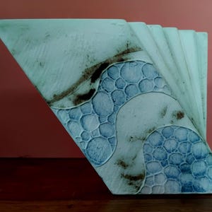 May include: A ceramic sculpture with a fan-like design. The sculpture features a triangular shape with a textured surface and a pattern of blue bubbles. The colors are primarily light blue, with brown and darker blue accents.