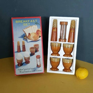 May include: A vintage breakfast set in a box labelled "BREAKFAST SET". The set includes wooden egg cups, salt and pepper shakers, and a timer. The box is red with a picture of bread. The set is in a white tray.