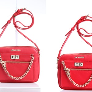 May include: A bright red crossbody bag with a gold-tone chain accent, a front zippered pocket, and a turn-lock closure. The bag features the text LOVE MOSCHINO in gold lettering on the front and includes an adjustable shoulder strap.