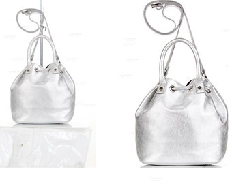 May include: A silver bucket bag with a drawstring closure and a long shoulder strap. The bag has a shiny, metallic finish.