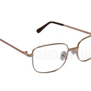 May include: A pair of gold-tone metal spectacles with clear lenses. The glasses have a square frame with a slightly rounded edge.