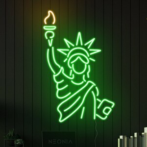 May include: Green neon sign of the Statue of Liberty with a yellow flame on the torch, mounted on a black wall above a desk with a laptop, a plant, and a chair. The text "NEONIA" is visible on the laptop screen. The text "COLOR SET 1" is visible in the upper right corner of the image.