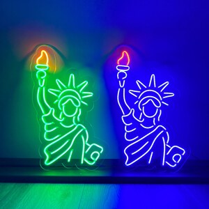 May include: Two neon signs depicting the Statue of Liberty, one in green and one in blue. The signs are lit up and have a glowing effect.