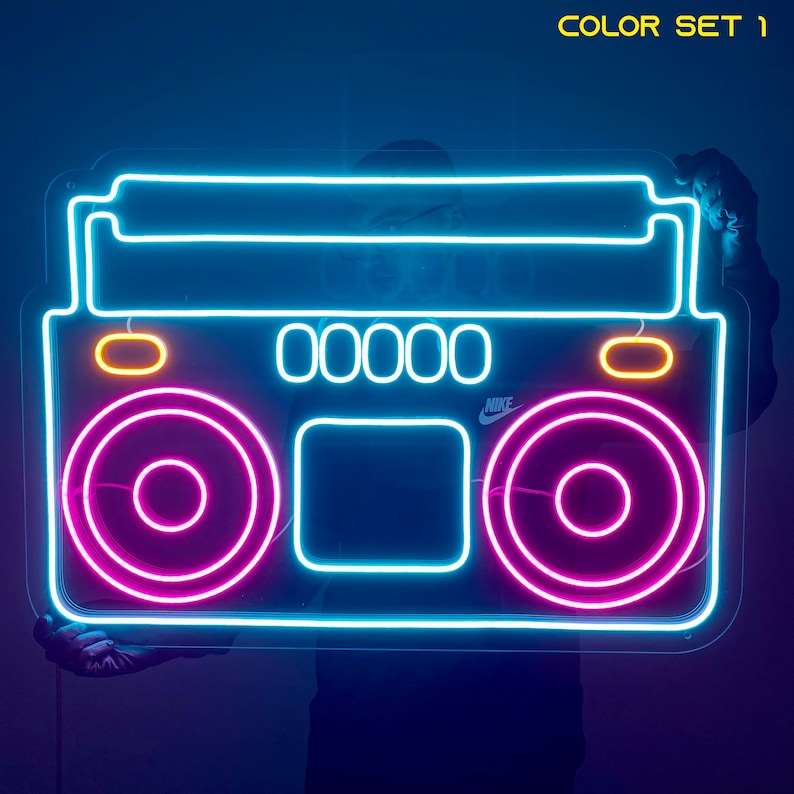 K&ouml;nnte beinhalten: Neon-Schild in Form eines Boombox mit blauen, rosa und gelben Lichtern. Das Schild tr&auml;gt die Aufschrift "NIKE" auf der Vorderseite.