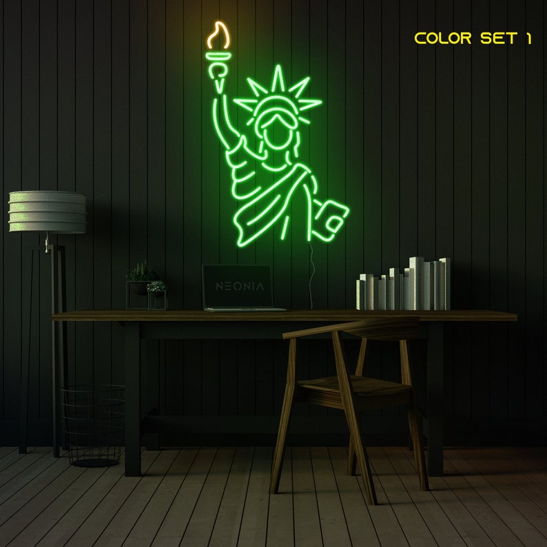May include: Green neon sign of the Statue of Liberty with a yellow flame on the torch, mounted on a black wall above a desk with a laptop, a plant, and a chair. The text "NEONIA" is visible on the laptop screen. The text "COLOR SET 1" is visible in the upper right corner of the image.