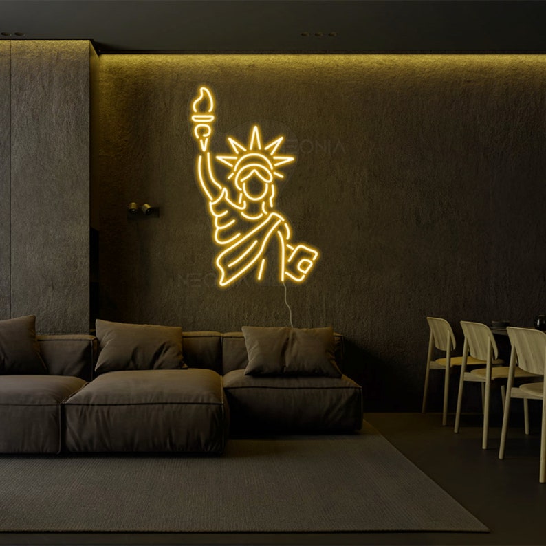 May include: A yellow neon sign depicting the Statue of Liberty, mounted on a dark wall in a living room setting. The sign is illuminated and casts a warm glow on the surrounding furniture.
