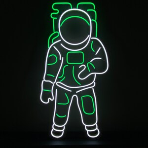 May include: Green neon astronaut sign with white outline. The astronaut is wearing a space suit with a helmet. The sign is on a black base.