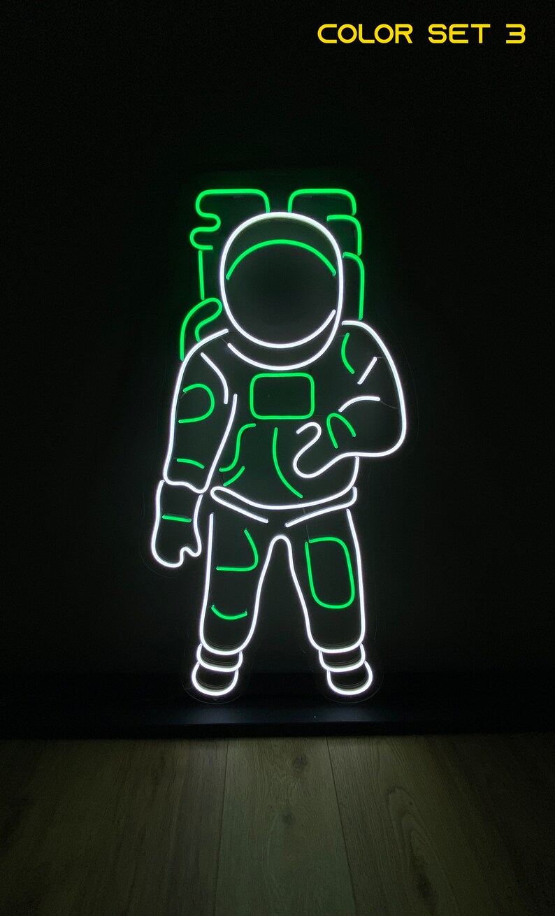 May include: Green neon astronaut sign with white outline. The astronaut is wearing a space suit with a helmet. The sign is on a black base.