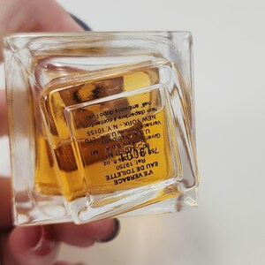 Puede incluir: Un frasco rectangular transparente de VE VERSACE Eau de Toilette. El frasco contiene un l&iacute;quido de color dorado. La etiqueta incluye el nombre de la marca, el tipo de producto y el volumen de 75 ml.