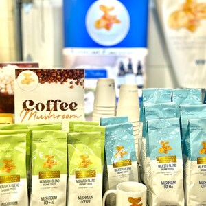 May include: A variety of coffee bags with the text "Great Lakes Mushroom Company" and "Mushroom Coffee" on the front. The bags are arranged on a table with a white mug with the same logo and a mushroom design.