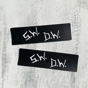 May include: Two black rectangular stickers with white text that reads "S.W. D.W."