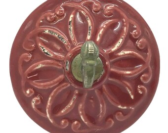 May include: A red ceramic bottle stopper with a floral design and a metal hook. The hook is in the center of the stopper and is attached to a metal ring.