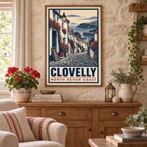 May include: A framed wall art print featuring a vintage-style illustration of a cobblestone street in Clovelly, North Devon Coast. The image depicts white cottages adorned with red flowers, a lantern, and a view of the sea in the background.