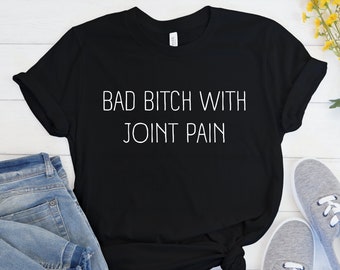 May include: Black t-shirt with white text that reads "Bad Bitch With Joint Pain".